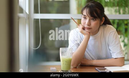 Portrait d'une jeune femme adolescente regardant par la fenêtre tout en faisant du travail à la maison dans un café Banque D'Images