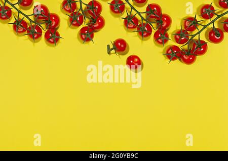Petits pains de tomates cerises brillantes en lumière dure avec ombre sur fond jaune, plat, bordure, espace de copie. Motif de cuisine coloré. Banque D'Images