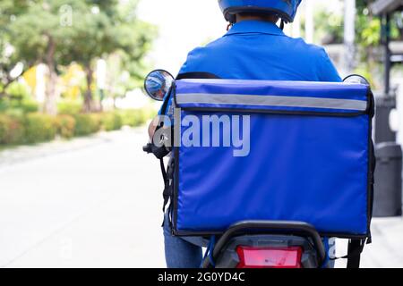 Le liveur porte une moto bleue uniforme et une boîte de livraison. Moto fournissant un service express de nourriture ou de colis Banque D'Images