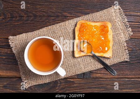 Tasse à thé et pain grillé à la confiture d'abricot sur une table en bois, vue du dessus Banque D'Images