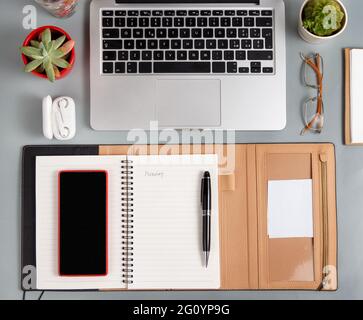 Ordinateur portable, téléphone portable et agenda ouvert sur un bureau gris vue sur le dessus. Concept d'entreprise Banque D'Images