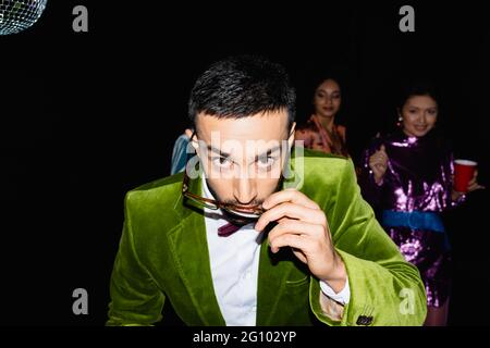 jeune homme arabe adulte qui règle des lunettes tout en ayant la fête avec des amis multiraciaux sur fond noir Banque D'Images