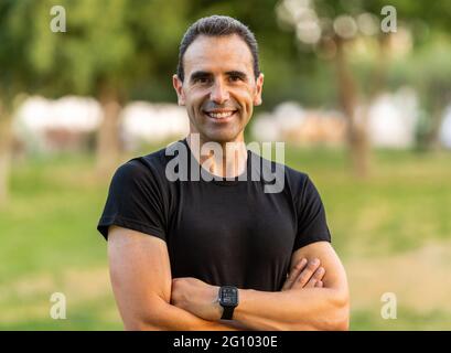 Homme adulte portant des vêtements de sport noirs croisant les bras et regardant l'appareil photo. Il sourit. Banque D'Images
