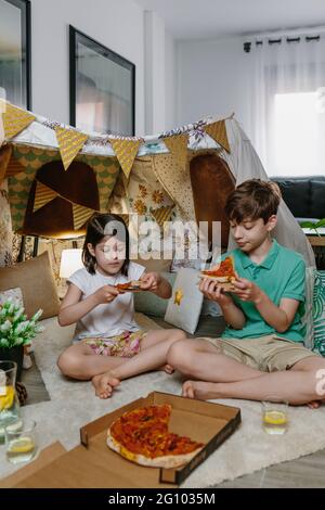 Les enfants qui mangent de la pizza et de la limonade en campant à la maison Banque D'Images