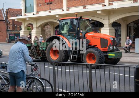 Route principale du village de Wroxham à l'extérieur des roys avec un tracteur agricole équipé d'un équipement de coupe de l'herbe en passant Banque D'Images