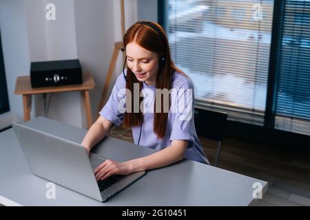 Vue de dessus d'une jeune femme opérateur attrayante utilisant un casque et un ordinateur portable pendant l'assistance à la clientèle au bureau à domicile. Banque D'Images