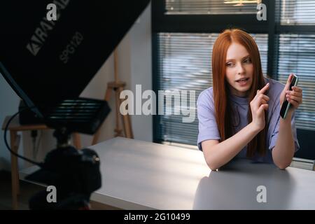 Webcam vue de la jeune femme souriante blogger saluant les suiveurs et parler du téléphone pendant le chat vidéo sur l'arrière-plan de la fenêtre. Banque D'Images