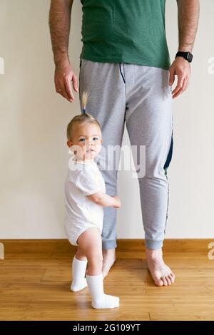 La petite fille se tient à la jambe de papa dans la chambre Banque D'Images