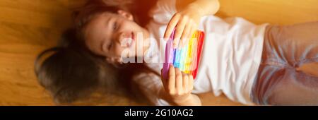 anti stress sensory pop it jouets dans les mains d'un enfant. une petite fille heureuse joue avec un simple jouet à fossettes à la maison. tout-petit tenant et jouant à la pop Banque D'Images
