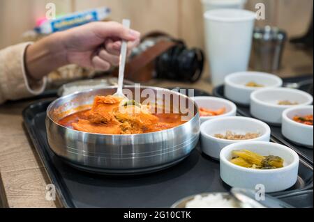 À la main, utilisez une cuillère pour ramasser de la soupe aux kimchi épicée et du pickle aux légumes sur une tasse au restaurant Banque D'Images