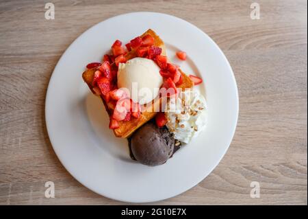 Toast au miel avec fraise en tranches, vanille, glace au chocolat noir et crème fouettée dans une assiette blanche Banque D'Images