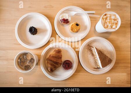 Vue de dessus de Croissant, Banoffee, Scone, Canele sur une assiette en papier et café glacé sur une table en bois dans le café Banque D'Images