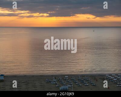 Vue aérienne sur le ciel pittoresque et coloré avec coucher de soleil derrière les nuages au-dessus de la mer méditerranée et plage avec chaises longues. Banque D'Images
