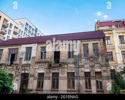 L'extérieur d'un vieux bâtiment en briques abandonné de deux étages à moitié ruiné à l'ombre d'une nouvelle tour fraîchement construite dans le centre de la ville de Kiev, en Ukraine. Banque D'Images