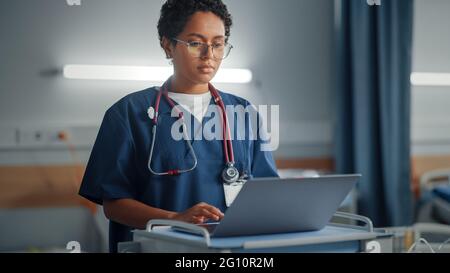 Hôpital: Professionnel souriant Noir la tête de la femme infirmière ou le docteur portant le stéthoscope utilise l'ordinateur médical. Dans la zone patients en arrière-plan dans les lits Banque D'Images
