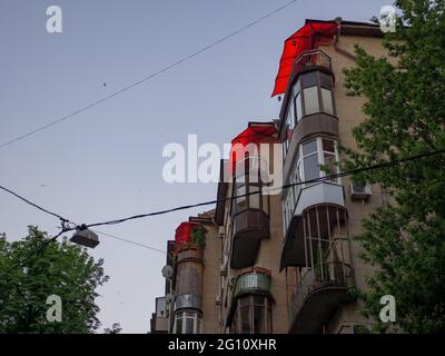 Le mur extérieur en brique d'un ancien bâtiment de l'époque soviétique avec de beaux balcons avec des stores rouges ouverts au soleil dans le centre de la ville de Kiev. Banque D'Images