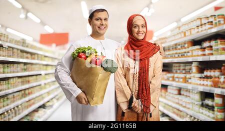 Un jeune couple musulman dans un supermarché tenant un sac de shopping en papier avec des provisions et posant Banque D'Images