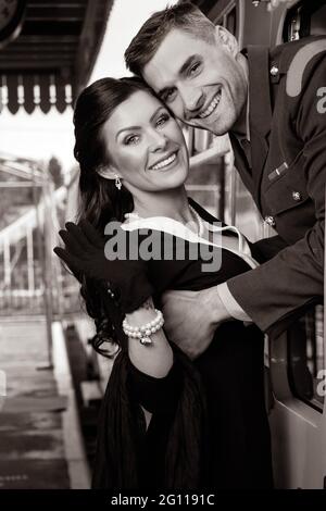 Vintage couple, homme en uniforme, femme en robe noire et se tenant les uns les autres sur le train, souriant et regardant la caméra. Banque D'Images