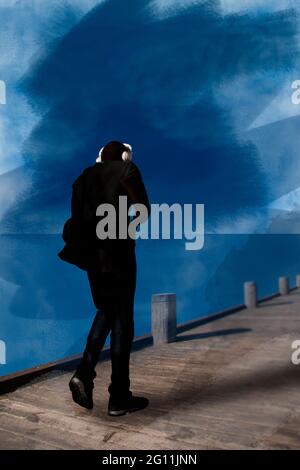 Image aquarelle d'un homme noir avec des écouteurs blancs marchant sur une promenade en bois au bord de la mer. Vue de derrière. Image générée par ordinateur. Banque D'Images