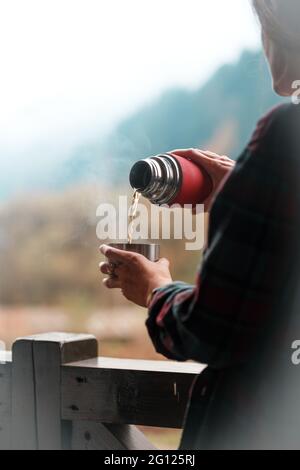 Une fille verse le thé d'un thermos sur un fond de montagnes Banque D'Images