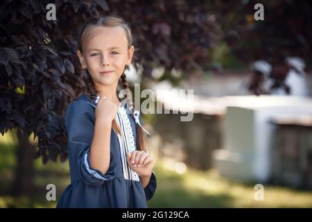 Charmante petite fille dans une robe rétro marchant dans la ville un jour d'été ensoleillé. Petite fille porte l'uniforme d'école. Fille d'école primaire avec de longs cheveux. Banque D'Images