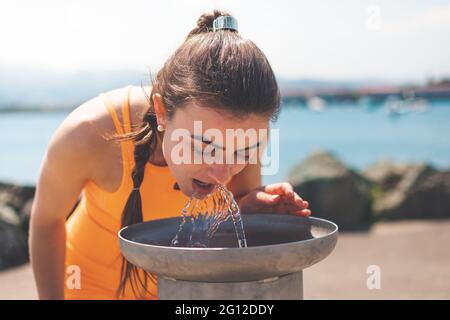 Une jeune femme de race blanche boit de l'eau à une fontaine du parc Banque D'Images