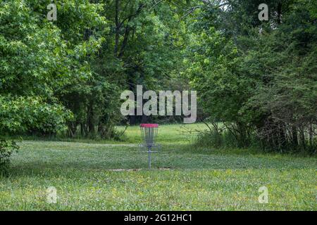 Panier de golf à disque rouge avec chaînes dans un cadre rustique dans les bois sur un parcours dans le parc vide lors d'une chaude journée ensoleillée au printemps Banque D'Images