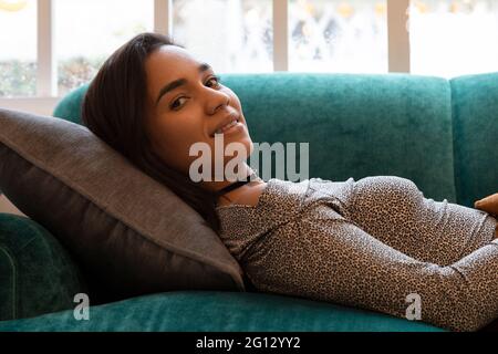 dans une chambre, une jeune femme latine avec des cheveux courts est couché sur un canapé coloré et un oreiller, se reposer et sourire, style de vie Banque D'Images