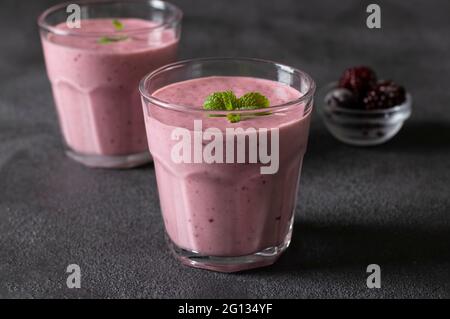 Smoothies faits maison aux mûres glacées dans deux verres transparents sur fond gris foncé. Banque D'Images