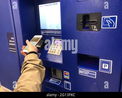 Parking payant à la station payante, parking payant à un guichet automatique. Une personne utilisant un terminal et un smartphone avec PayPass. Une main insérant une étiquette dans la fente Banque D'Images