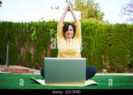 Une femme prend un cours de yoga à l'extérieur de son ordinateur portable Banque D'Images