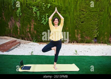 Une femme prend un cours de yoga à l'extérieur de son ordinateur portable Banque D'Images