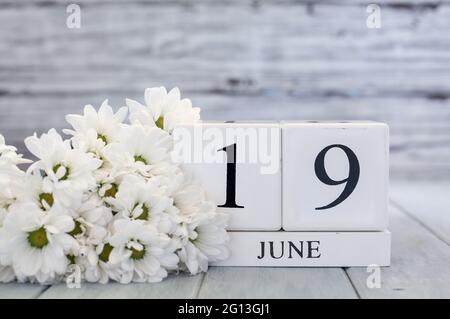 Le dix-septième blocs de calendrier en bois blanc avec la date du 19 juin et les pâquerettes blanches. Mise au point sélective avec arrière-plan flou. Banque D'Images