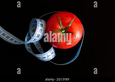 La tomate et un mètre ruban bleu sur fond noir, concept de saine alimentation et de nutrition Banque D'Images