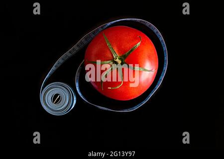 La tomate et un mètre ruban bleu sur fond noir, concept de saine alimentation et de nutrition Banque D'Images