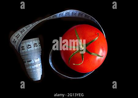 La tomate et un mètre ruban bleu sur fond noir, concept de saine alimentation et de nutrition Banque D'Images