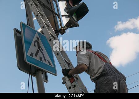 Dnepropetrovsk, Ukraine - 05.30.2021: Les travailleurs des services publics de la ville peinent un feu de circulation. Un employé effectue un travail dangereux pendant Banque D'Images