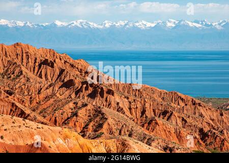 Formations rocheuses rouges avec le lac Issyk Kul en arrière-plan à Kaji Say, au Kirghizistan. Banque D'Images