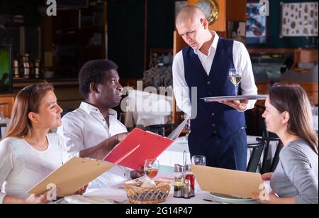 serveuse positive qui commande aux clients au café Banque D'Images
