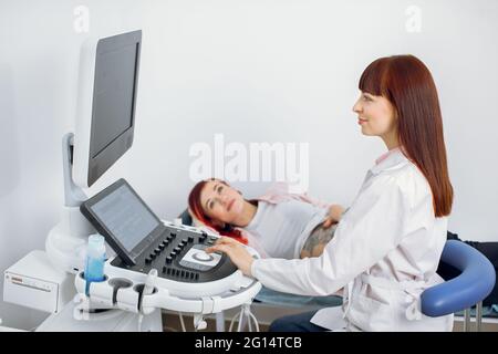 Portrait d'une femme professionnelle hautement qualifiée médecin obstétricien caucasien examinant la femme enceinte par échographie. Femme enceinte ayant le dépistage ultrasonique dans une clinique médicale moderne Banque D'Images