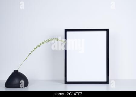 Image de maquette noire vide. Vase en céramique noire de forme irrégulière avec lame d'herbe. Bureau blanc et fond blanc Banque D'Images