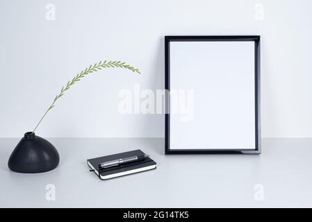 Image de maquette noire vide. Vase en céramique noire de forme irrégulière avec lame d'herbe. Bloc-notes noir et stylo élégant sur bureau blanc. Travaux modernes Banque D'Images