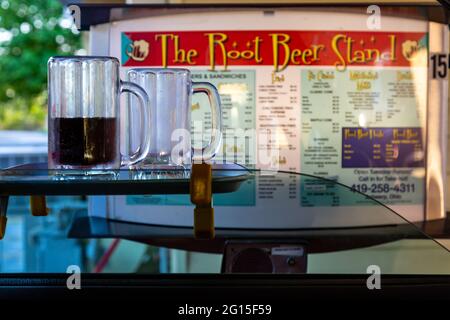 Un tableau de menu de drive-in se dresse au-delà de deux tasses, une à moitié pleine, assis sur un plateau sur la fenêtre d'un véhicule au Root Beer Stand à Anvers, Ohio, États-Unis. Banque D'Images