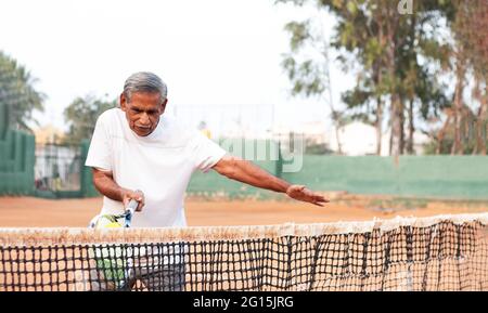 Homme âgé pratiquant le tennis près du filet - concept de personnes âgées actives en bonne santé et en forme. Banque D'Images