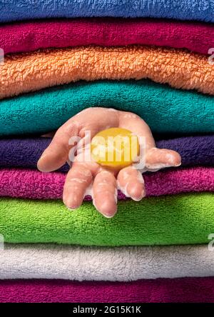 Femme tenant le savon à la main entre les serviettes propres. Savon naturel jaune dans la main de la femme contre un fond de serviettes multicolores Banque D'Images