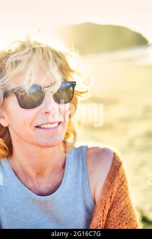 Portrait d'une jeune femme de race blanche, blonde et mûre, avec des lunettes de soleil à l'extérieur sur une plage. Banque D'Images