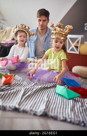 Un jeune père s'amusant à jouer sur le sol avec ses petites filles dans une atmosphère détendue à la maison. Famille, maison, jeux Banque D'Images