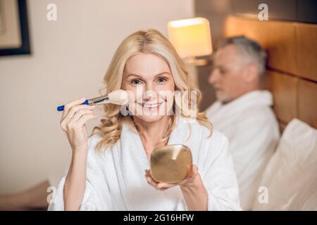 Mignonne blonde femme faisant le maquillage et l'air heureux Banque D'Images