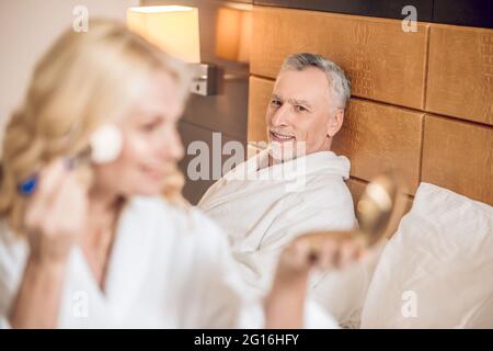 Mignonne blonde femme faisant le maquillage et l'air heureux Banque D'Images