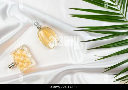 Parfum pour femmes sur soie blanche avec feuilles vertes Banque D'Images